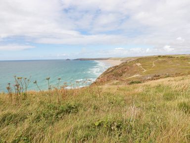 A coastal landscape with grassy cliffs and a sandy beach along the ocean at Sandpiper in Perranporth