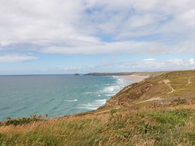 A coastal landscape with cliffs grassy fields paths and ocean waves at Sandpiper in Perranporth
