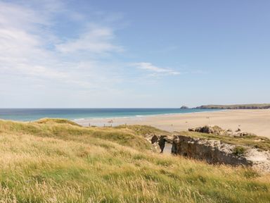 A sandy beach with waves and grassy dunes in the foreground at Sandpiper in Perranporth