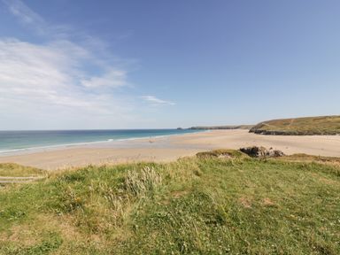 A view of a sandy beach with the sea and a grassy cliff in the foreground at Sandpiper in Perranporth