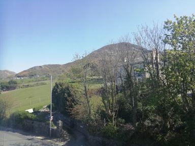 A road with a 40 speed limit sign and trees near a house with hills and fields in the background at Llys Madoc The Top Flat in Penmaenmawr