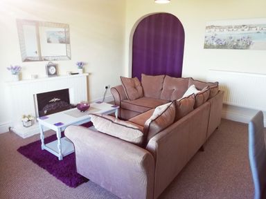A living room with two sofas a white coffee table and a fireplace with a mirror above at Llys Madoc The Top Flat in Penmaenmawr