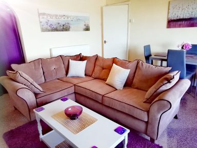 A living room with a brown sectional sofa white coffee table and a dining table with chairs at Llys Madoc The Top Flat in Penmaenmawr