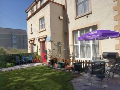 An outdoor patio area with chairs tables potted plants and an umbrella outside a building with a red door at Llys Madoc The Top Flat in Penmaenmawr