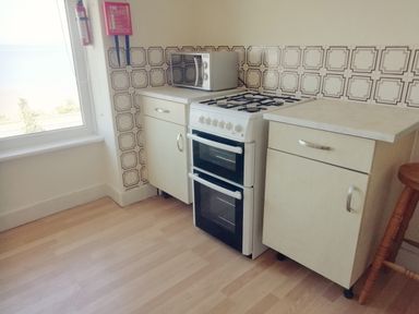 A kitchen corner with a gas stove, microwave on a counter, fire safety equipment on the wall, and cabinets at Llys Madoc The Top Flat in Penmaenmawr