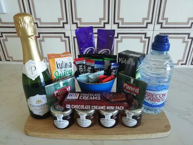 A selection of beverages snacks and condiments including a bottle of sparkling wine juice bottled water chocolates biscuits and jars of jam at Llys Madoc The Top Flat in Penmaenmawr