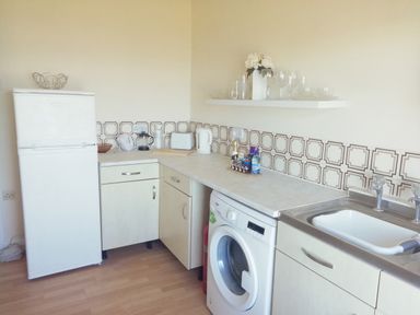 A kitchen with a refrigerator washing machine sink countertop and shelves with glassware at Llys Madoc The Top Flat in Penmaenmawr