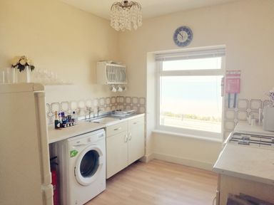A kitchen with a washing machine sink stove and window showing a view at Llys Madoc The Top Flat in Penmaenmawr