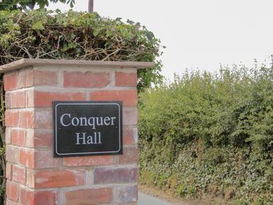 A brick pillar with a sign reading Conquer Hall next to a hedge at Hendomen near Montgomery
