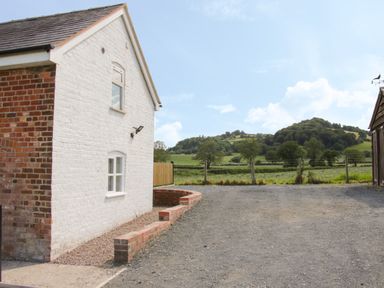 Exterior of a white brick house with windows and a gravel driveway overlooking green hills and fields at Conquer Hall in Hendomen near Montgomery