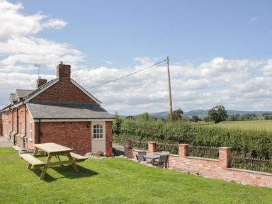 A brick house with a wooden picnic table on the grass and a patio set near a brick fence at Conquer Hall in Hendomen near Montgomery