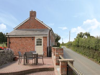 An outdoor patio with a table and four chairs next to a brick house along a country road at Conquer Hall in Hendomen near Montgomery