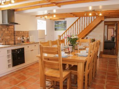 A kitchen and dining area with a wooden dining table set for eight and kitchen appliances at Conquer Hall in Hendomen near Montgomery