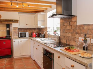 A kitchen with white cabinets a red stove microwave kettle and food on the countertop at Conquer Hall in Hendomen near Montgomery