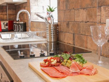 A kitchen countertop with a cutting board holding sliced meats olives greens and sun dried tomatoes next to a stovetop and a clear glass at Conquer Hall in Hendomen near Montgomery