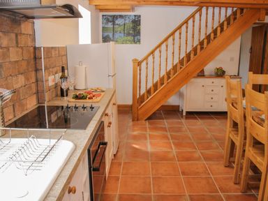 A kitchen with a stove sink and countertop near a wooden staircase and dining table at Conquer Hall Hendomen near Montgomery