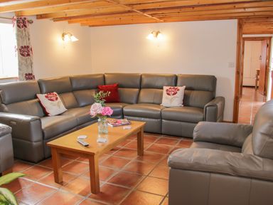 A living room with a gray sectional sofa and armchair a wooden coffee table with flowers and magazines on tile floor at Conquer Hall in Hendomen near Montgomery