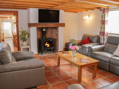 A living room with leather sofas a wooden coffee table a fireplace with a fire and a television mounted above at Conquer Hall in Hendomen near Montgomery
