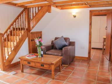 A sitting area with a leather armchair and wooden coffee table with flowers and books near a wooden staircase at Conquer Hall in Hendomen near Montgomery