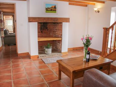 A sitting area with a wooden coffee table holding flowers and a wine bottle beside a brick fireplace at Conquer Hall in Hendomen near Montgomery
