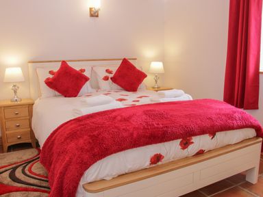 A bedroom with a bed with red pillows and a red throw with bedside tables and lamps at Conquer Hall in Hendomen near Montgomery