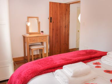 A bedroom with a wooden dressing table with mirror and stool a red blanket and folded towels on the bed at Conquer Hall in Hendomen near Montgomery