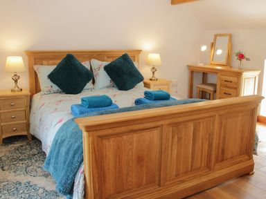 A bedroom with a wooden bed, bedside tables with lamps, a wooden dressing table with a mirror and flowers at Conquer Hall in Hendomen near Montgomery