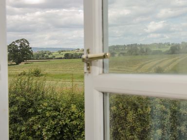 A view through a partially open window showing fields with mowed lines bushes and trees at Conquer Hall in Hendomen near Montgomery