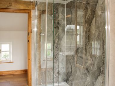 A bathroom with a glass shower enclosure and marble wall tiles at Conquer Hall in Hendomen near Montgomery