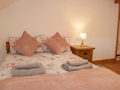 A bedroom with a bed with floral sheets and pink pillows next to a wooden nightstand with a lamp at Conquer Hall Hendomen near Montgomery