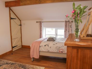 A bedroom with a bed folded towels a wooden dresser with flowers and a window with curtains at Conquer Hall in Hendomen near Montgomery