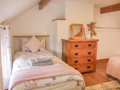 A bedroom with a single bed with floral bedding and folded towels on it a wooden chest of drawers with a mirror and flowers on top at Conquer Hall in Hendomen near Montgomery