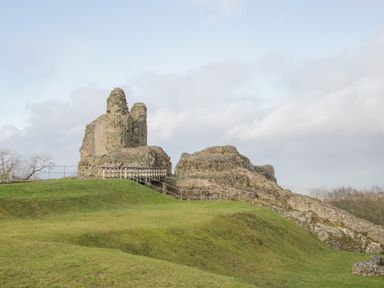 Ruins of a stone castle on a grassy hill with a wooden bridge and railings at Conquer Hall in Hendomen near Montgomery
