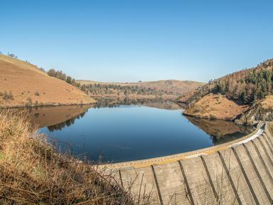 A dam with water held back by hills and trees at Conquer Hall in Hendomen near Montgomery