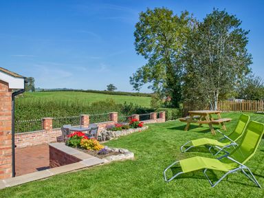 A garden with green lawn chairs, a wooden picnic table, flowers, and a patio area at Conquer Hall in Hendomen near Montgomery