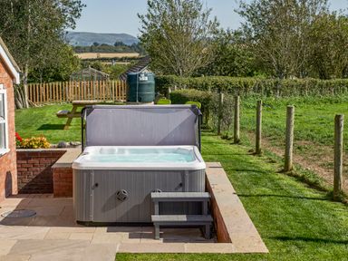 A garden with a hot tub on a paved area next to a grassy lawn and a wooden fence at Conquer Hall in Hendomen near Montgomery