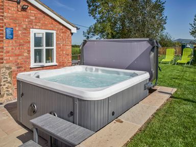 An outdoor hot tub with water next to a brick building and two yellow lounge chairs on grass at Conquer Hall Hendomen near Montgomery