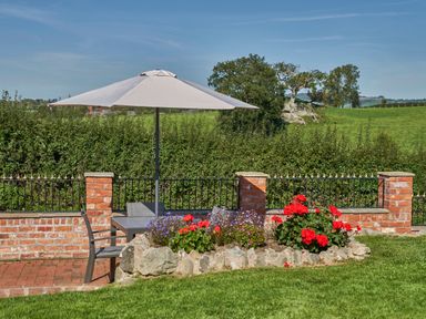 An outdoor seating area with a table and umbrella next to a flower bed and brick wall at Conquer Hall in Hendomen near Montgomery