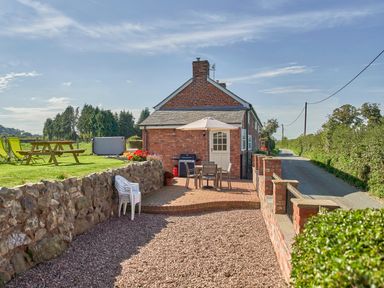A brick house with a small patio table and umbrella and plastic chairs by a country road at Conquer Hall in Hendomen near Montgomery