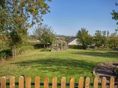 A fenced grassy garden with a glass greenhouse and trees at Conquer Hall in Hendomen near Montgomery