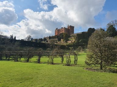 A castle on a hill with trimmed shrubs and green grass in the foreground at Conquer Hall in Hendomen near Montgomery