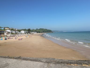 A sandy beach with people and houses along the shore at 2 Primrose Cottage in Saundersfoot