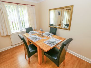 A dining room with a wooden table set for four with black chairs a large mirror on the wall and a window with white curtains at 2 Primrose Cottage in Saundersfoot