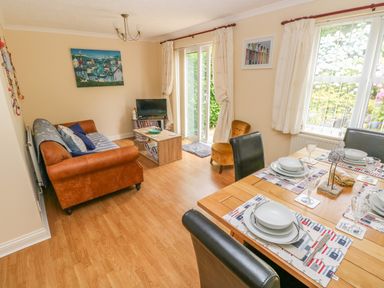 A living and dining area with a brown sofa a wooden dining table set for four and sliding glass doors at 2 Primrose Cottage Saundersfoot