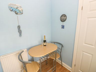 A small dining area with a wooden table and two chairs with a bottle and two glasses on the table at 2 Primrose Cottage in Saundersfoot