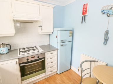 A kitchen corner with a gas stove, oven, light blue refrigerator, kettle, small round table and chair at 2 Primrose Cottage in Saundersfoot