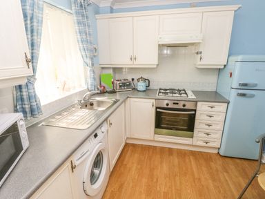 A kitchen with white cabinets a washing machine a stainless steel sink a microwave oven a toaster a kettle a gas stove an oven and a blue refrigerator at 2 Primrose Cottage in Saundersfoot