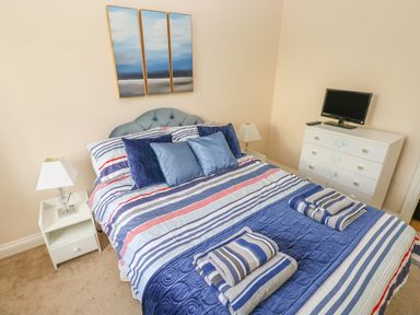A bedroom with a double bed with striped bed linen bedside tables with lamps a chest of drawers with a TV and a triptych painting on the wall at 2 Primrose Cottage Saundersfoot