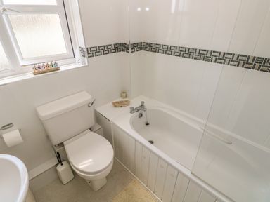 A bathroom with a toilet next to a bathtub with tiled walls and a window at 2 Primrose Cottage Saundersfoot