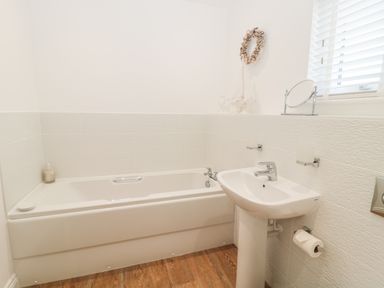 A bathroom with a bathtub and pedestal sink with a mirror and toilet paper holder at Waterside in Beadnell